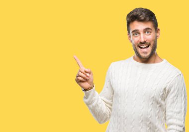 Kameraya bakarak yan el ve parmak ile işaret yüzünde kocaman bir gülümseme ile izole arka plan üzerinde kış kazak giyen genç yakışıklı adam.