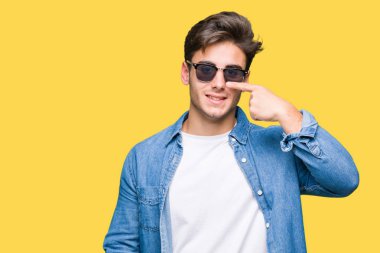 Genç yakışıklı adam giyen güneş gözlüğü izole üzerinde işaretleme için yüz ve burun, neşeli gülümseyerek el parmak ile arka plan