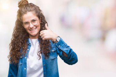 Güzel genç esmer kıvırcık saçlı kız mutlu yaşasın el ile jest yapıyor izole arka plan üzerinde gözlük takıyorum. Kameraya bakarak başarı gösteren ile ifade onaylama.