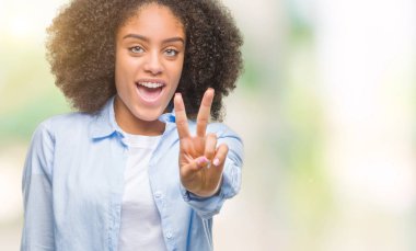 Mutlu yüz zafer işareti yaparken kameraya göz kırpıyor ile gülümseyen izole arka plan üzerinde genç afro Amerikalı kadın. İki numaralı.