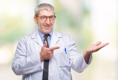 Yakışıklı kıdemli Doktor, hayret ve el ile sunulması ve parmak ile işaret ederken kameraya gülümseyen arka plan üzerinde beyaz önlük giyen bilim adamı profesyonel adam izole.