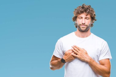 Yakışıklı İspanyol modeli adam ile gülümseyen izole arka plan üzerinde kapalı gözler ve yüzünde minnettar jest ile göğüs üzerinde eller. Sağlık kavramı.