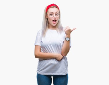 Seyir ve başparmak yanında yukarıyı mutlu yüz ile gülümseyen izole arka plan üzerinde gözlüklü sarışın genç kadın.