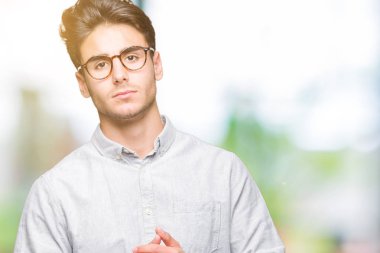 Arka plan eller üzerinde gözlük takan genç yakışıklı adam birlikte izole ve rahat ve neşeli gülümseyen parmak çarpı işareti. Başarı ve iyimser