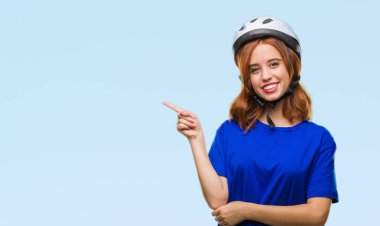 Kameraya bakarak yan el ve parmak ile işaret yüzünde kocaman bir gülümseme ile izole arka plan üzerinde bisikletçi kask giyen genç güzel kadın.