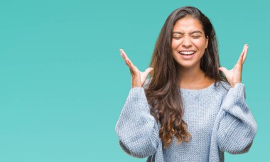 Üzerinde kış kazak giyen genç güzel Arap kadın deli ve çılgın çığlık kaldırdı ve kapalı gözleri heyecanlı silah ile başarı için arka plan kutlama izole. Kazanan kavramı