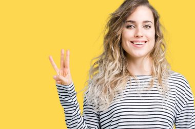 Güzel sarışın genç kadın giyiyor çizgili süveter gösterilen ve parmakları ile işaret izole arka plan üzerinde üçüncü ise kendinden emin ve mutlu gülümseyerek.