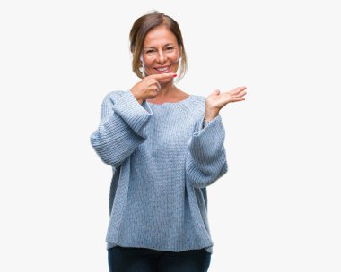 Hayret ve el ile sunulması ve parmak ile işaret ederken kameraya gülümseyen izole arka plan üzerinde kış kazak giyen orta yaş üst düzey İspanyol kadın.