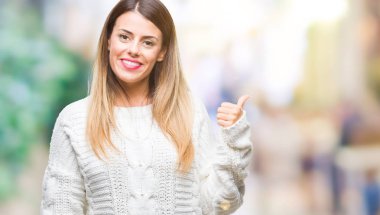 Genç güzel kadın rahat beyaz kazak seyir ve başparmak yanında yukarıyı mutlu yüz ile gülümseyen izole arka plan üzerinde.