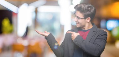 Genç yakışıklı zarif adam gözlüklü üzerinden hayran ve el ile sunulması ve parmak ile işaret ederken kameraya gülümseyen izole arka plan.