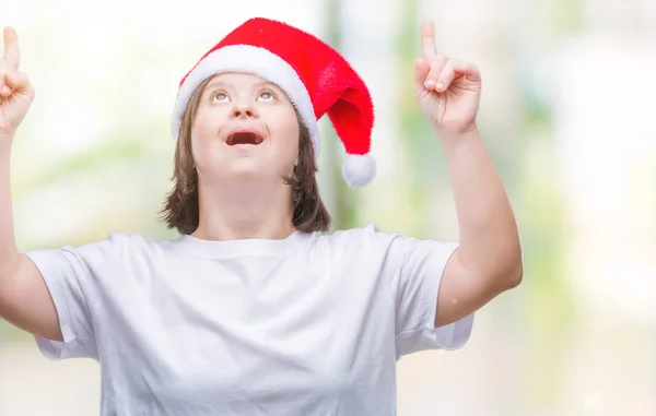 孤立した背景にクリスマス帽子をかぶっているダウン症候群の若い成人女性びっくりし 驚き見て 指で指して 腕を上げた — ストック写真