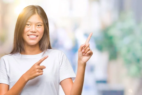 年轻的亚洲女人在孤独的背景上微笑着看着摄像机 用双手和手指指向旁边 — 图库照片