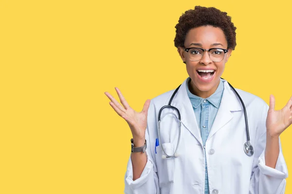 年轻的非洲医生妇女穿着医疗外套在孤立的背景庆祝疯狂和惊讶的成功与手臂抬起和睁开眼睛尖叫兴奋 优胜者概念 — 图库照片