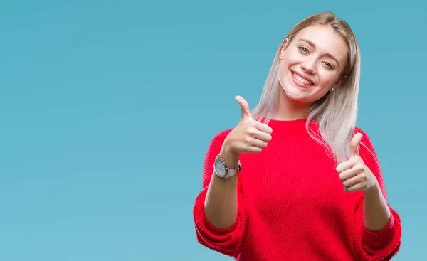 年轻的金发女人穿着冬季毛衣在孤立的背景下批准做积极的手势与手 竖起大拇指微笑 并为成功而高兴 看着相机 胜利者的手势 — 图库照片