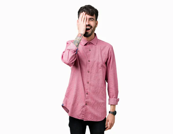年轻的帅哥穿着粉红色的衬衫在孤立的背景覆盖着一只眼睛用自信的微笑在脸上和惊喜的情感 — 图库照片