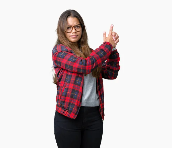 Young beautiful brunette woman wearing jacket and glasses over isolated background Holding symbolic gun with hand gesture, playing killing shooting weapons, angry face