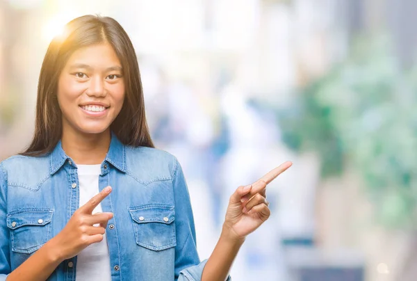 年轻的亚洲女人在孤独的背景上微笑着看着摄像机 用双手和手指指向旁边 — 图库照片