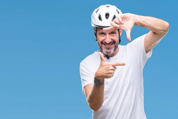 Middle age senior hoary cyclist man wearing bike safety helment isolated background smiling making frame with hands and fingers with happy face. Creativity and photography concept.