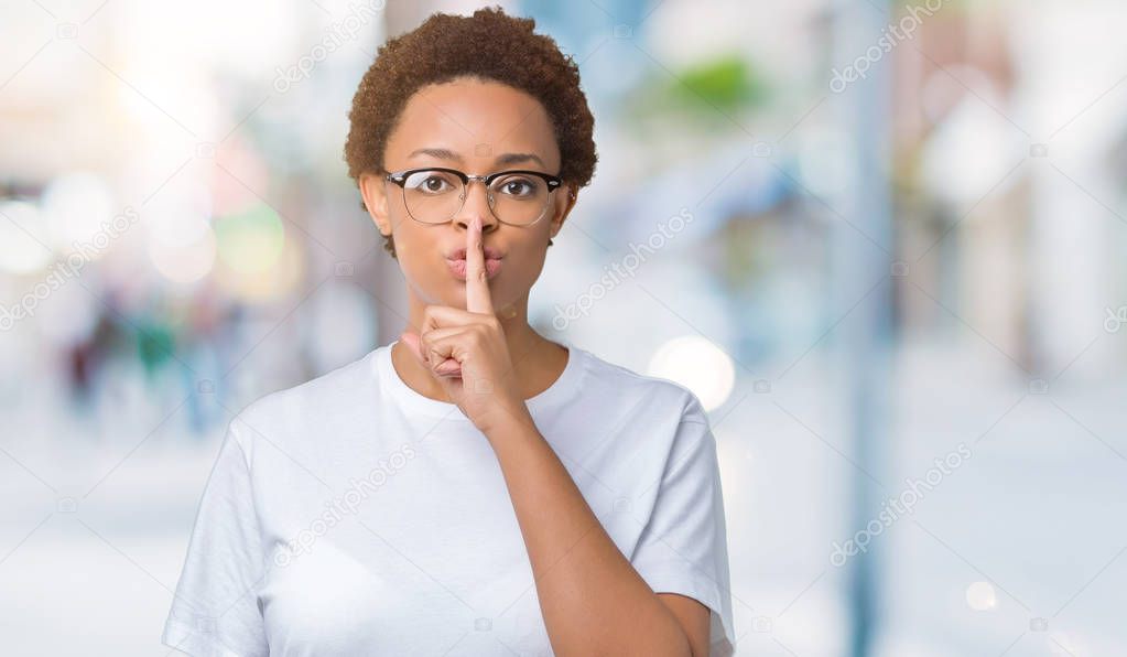 Beautiful young african american woman wearing glasses over isolated background asking to be quiet with finger on lips. Silence and secret concept.
