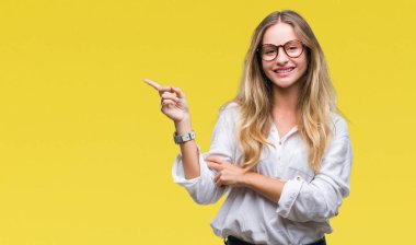 Yüzünde kocaman bir gülümseme ile izole arka plan üzerinde gözlük takan genç güzel sarışın iş kadını kameraya bakarak yan el ve parmak ile işaret.