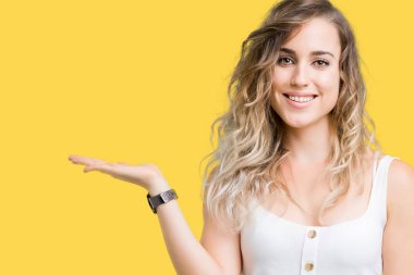 Neşeli sunulması ve kameraya bakarak avucunun ile işaret gülümseyen izole arka plan genç güzel sarışın kadın.