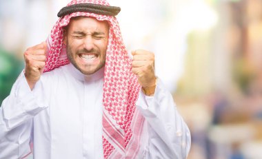 Zafer kutluyor gülümseyen izole arka kolları olan başarı için heyecan üzerinde keffiyeh giyen genç yakışıklı adam kaldırdı. Kazanan kavramı.