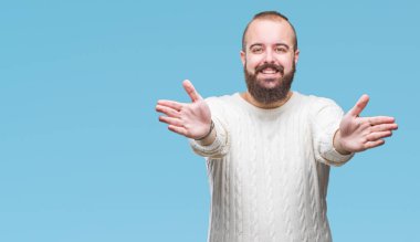 Sarılmak için kollarını açarak gülümseyerek kameraya bakarak izole arka plan üzerinde kış kazak giyen genç beyaz hipster adam. Neşeli ifade kucaklayan mutluluk.