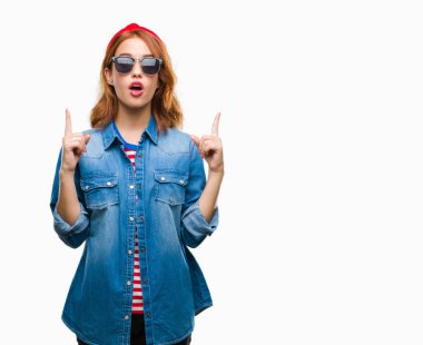 Genç güzel kadın güneş gözlüğü takıyor izole arka plan üzerinden hayran ve yukarıya bakıyor ve parmakları ile işaret ve silah kaldırdı şaşırttı.