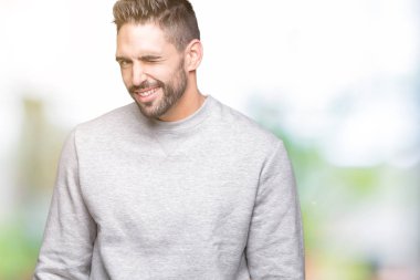 Seksi bir ifadeyle, neşeli ve mutlu yüzünü kameraya bakarak göz kırpıyor izole arka plan üzerinde sweatshirt giyen genç yakışıklı adam.