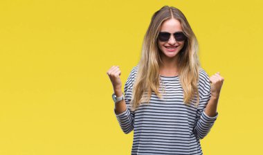 Genç güzel sarışın kadın üzerinde güneş gözlüğü takıyor arka plan çok mutlu ve heyecanlı kaldırdı, silah ile kazanan jest yapıyor gülümseyen ve başarı için çığlık izole. Kutlama kavramı.