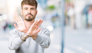 İzole arka plan ret ifade geçiş silah ve avuç içi eksi işareti, kızgın surat yapıyor üzerinde sweatshirt giyen genç yakışıklı adam