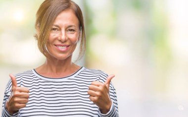 Orta yaş üzerinde el ile pozitif jest yapıyor izole arka plan başarı işareti İspanyol kadın kıdemli başparmak gülümseyen ve mutlu. Neşeli bir ifadeyle, kazanan jest kameraya bakıyor.