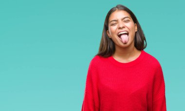 Dilini izole arka plan üzerinde kış kazak giyen genç güzel Arap kadın out komik ifade ile mutlu. Duygu kavramı.