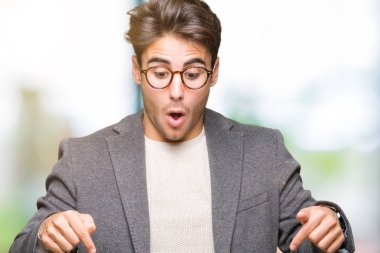 Genç iş adamı gözlük izole üzerinde işaretleme aşağı reklam, sürpriz yüz ve açık ağız gösterilen parmakları ile arka plan