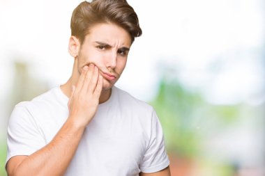 Diş ağrısı veya dişlerde dişlerle ilgili hastalık nedeniyle ağız acı ifadesi ile el ile dokunmak izole arka plan üzerinde beyaz t-shirt giyen genç yakışıklı adam. Diş hekimi kavramı.