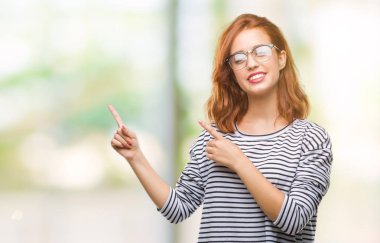 İzole arka plan gülümseyen ve iki elleri ve parmakları ile tarafına işaret kamera bakarak gözlüklü genç güzel kadın.