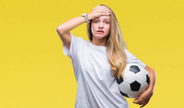 Futbol topu kafa üzerinde el ile vurguladı izole arka plan üzerinde tutan genç güzel sarışın kadın şok utanç ve sürpriz suratla, öfkeli ve sinirli. Korku ve hata için üzgün.