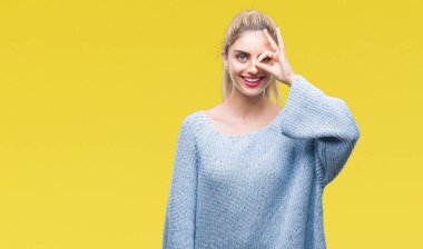 Gülümseyen, parmakları ile mutlu yüz üzerinden seyir göz el ile ok jest yapıyor izole arka plan üzerinde kış kazak giyen genç güzel sarışın ve mavi gözlü kadın.