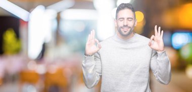 Genç yakışıklı adam giyen kazak izole arka plan üzerinde dinlenmek ve gülümseyen gözlerle parmak ile meditasyon jest yapıyor kapalı. Yoga kavramı.