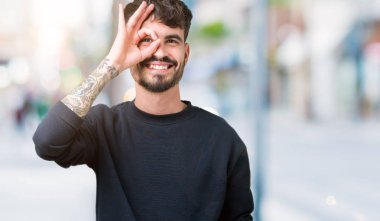 Genç yakışıklı adam gülümsüyor, parmakları ile mutlu yüz üzerinden seyir göz el ile ok jest yapıyor izole arka plan üzerinde.