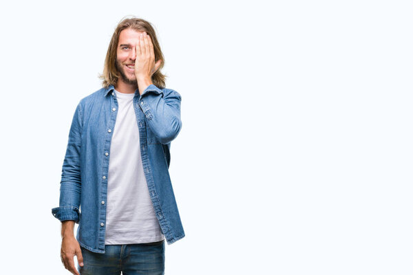 Young handsome man with long hair over isolated background covering one eye with hand with confident smile on face and surprise emotion.