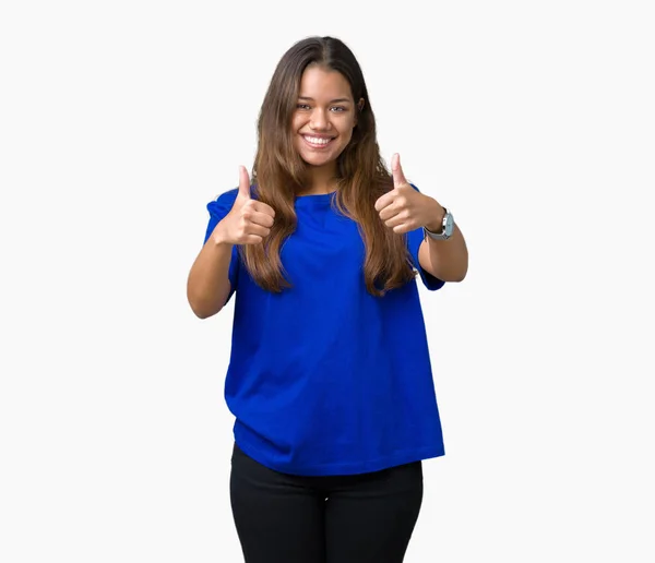 年轻美丽的黑发女人穿着蓝色 T恤在孤立的背景成功标志做积极的手势 竖起大拇指微笑和快乐 带着欢快的表情 获胜者的手势看着镜头 — 图库照片
