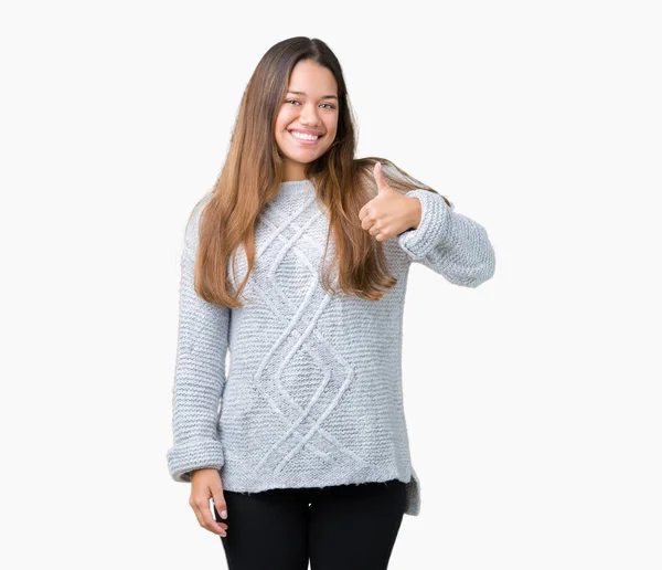 若い美しいブルネット女性の幸せの親指を手でジェスチャーをして孤立した背景の上にセーターを着ています 成功を示すと カメラを見て式を承認します — ストック写真