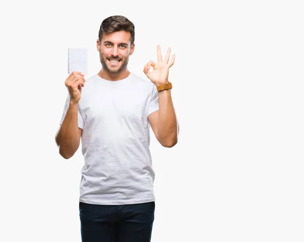 Joven Hombre Guapo Sosteniendo Cuaderno Sobre Fondo Aislado Haciendo Signo —  Fotos de Stock