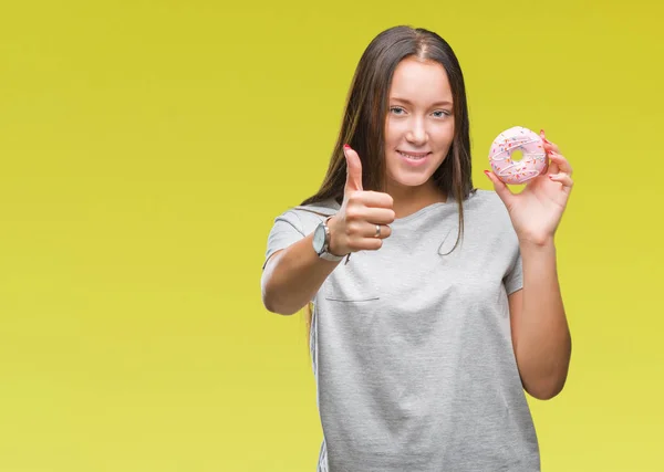 笑顔の サイン 優秀な兆候を親指をやって幸せな孤立の背景に甘いドーナツを食べる若い白人女性 — ストック写真