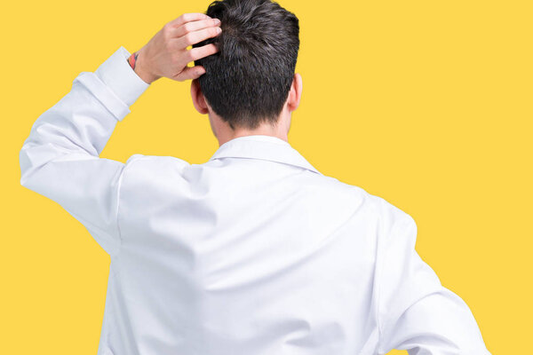 Молодой профессиональный ученый в белом халате на изолированном фоне задом наперед думает о сомнениях с рукой на голове
