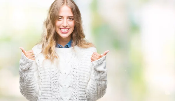 Beautiful young blonde woman wearing winter sweater over isolated background success sign doing positive gesture with hand, thumbs up smiling and happy. Looking at the camera with cheerful expression, winner gesture.