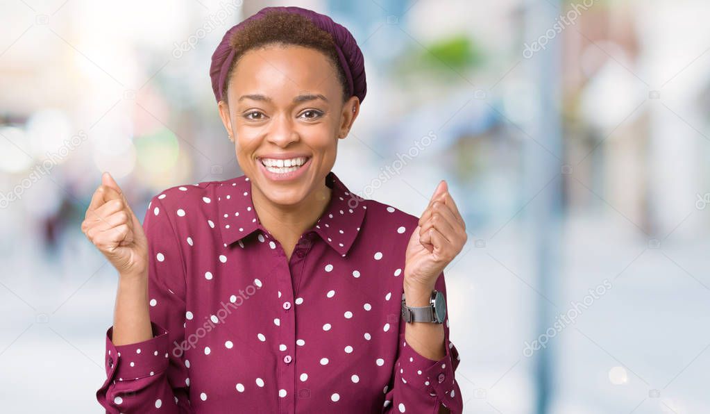 Beautiful young african american woman wearing head scarf over isolated background celebrating surprised and amazed for success with arms raised and open eyes. Winner concept.