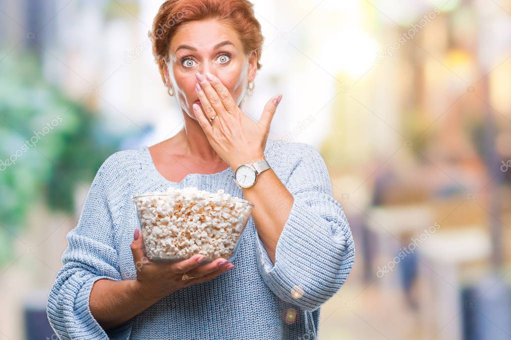 Atrractive senior caucasian redhead woman eating popcorn over isolated background cover mouth with hand shocked with shame for mistake, expression of fear, scared in silence, secret concept