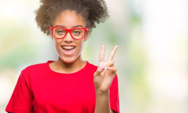 Mutlu yüz zafer işareti yaparken kameraya göz kırpıyor ile gülümseyen izole arka plan üzerinde gözlük takan genç afro Amerikalı kadın. İki numaralı.